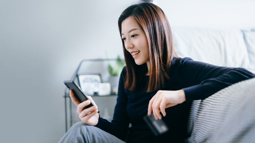 A woman is using a phone in bed; image used on HSBC Malaysia benefits of online banking article page.